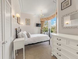 A bedroom with a metal bed frame white bedding a white dresser a window with curtains and a wall-mounted television at Fir Trees in Windermere