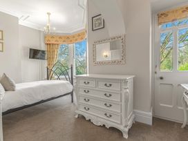 A bedroom with a metal framed bed white dresser a wall mirror and windows at Fir Trees in Windermere