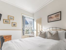 A bedroom with a white bed a window with curtains a wooden chair small wooden dresser and framed pictures on the walls at Fir Trees in Windermere