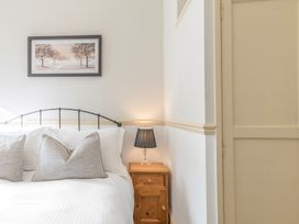 A bedroom corner with a bed white pillows a wooden bedside table with a lamp and a framed picture on the wall at Fir Trees in Windermere