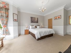 A bedroom with a double bed bedside tables lamps paintings and floral curtains at Fir Trees in Windermere
