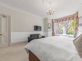 A bedroom with a bed a black sofa a wall mounted TV and windows with floral curtains at Fir Trees in Windermere