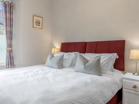 A bedroom with a large bed with white linens red headboard bedside tables lamps and a window with plaid curtains at Fir Trees in Windermere