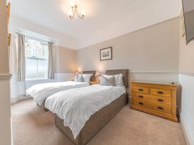 A bedroom with two single beds bedside tables lamps a window and a wooden chest of drawers at Fir Trees in Windermere
