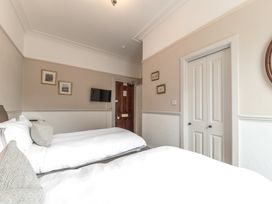 A bedroom with two beds pillows wall paintings a door and a television at Fir Trees in Windermere