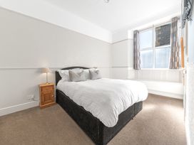 A bedroom with a double bed two pillows a wooden bedside table with a lamp a window with curtains and a wall-mounted television at Fir Trees in Windermere