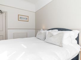 A bedroom with a double bed with white bedding and pillows a framed picture on the wall radiator and a closed door at Fir Trees in Windermere