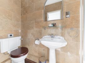A bathroom with a white toilet with a dark wooden seat a pedestal sink a mirror and toiletries on a glass shelf at Fir Trees in Windermere