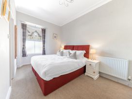 A bedroom with a red bed frame white bedding bedside table with lamp and window with curtains at Fir Trees in Windermere