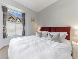 A bedroom with a large bed with white bedding and red headboard near a window with plaid curtains at Fir Trees in Windermere