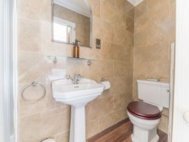 A bathroom with a pedestal sink a wall mirror and a toilet with a wooden seat at Fir Trees in Windermere