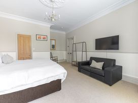 A bedroom with a bed a black sofa a wall mounted TV a wooden door and a chair at Fir Trees in Windermere