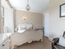 A bedroom with a white ornate bed a window with curtains a white wardrobe and a brown armchair at Fir Trees in Windermere