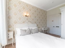 A bedroom with a double bed a white headboard bedside tables a desk patterned wallpaper and a door at Fir Trees in Windermere