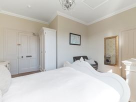 A bedroom with a white bed a white wardrobe a black armchair a wall mirror and a framed map at Fir Trees in Windermere