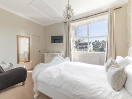 A bedroom with a white bed and chest of drawers near a window with curtains and a wall-mounted tv at Fir Trees in Windermere