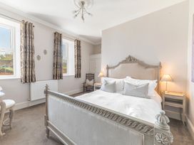 A bedroom with a large bed with white bedding two bedside tables lamps a chair and windows with curtains at Fir Trees in Windermere