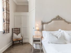 A bedroom corner with a wooden chair and cushion next to a nightstand with a lamp by a bed at Fir Trees in Windermere