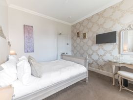 A bedroom with a bed white bedding a wall mounted television a dressing table and patterned wallpaper at Fir Trees in Windermere
