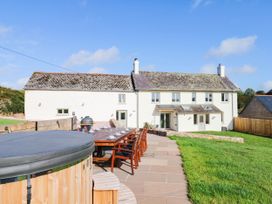 An outdoor area with a house, table, chairs, and a jacuzzi at Higher Weekaborough Farm in Coombe Fishacre near Ipplepen