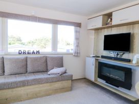 A seating area with a sofa under a large window and a wall-mounted television above an electric fireplace at 31A Foxburrow Hang in Fritton near Belton Norfolk