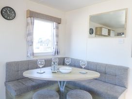 A dining nook with a wooden table chairs corner bench seating and a window with curtains at 31A Foxburrow Hang in Fritton near Belton Norfolk