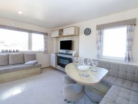 A living room with grey sofas a wooden table with glassware a wall-mounted television and fireplace at 31A Foxburrow Hang in Fritton near Belton Norfolk