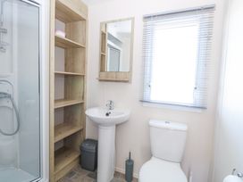 A bathroom with a shower enclosure sink toilet wooden shelves mirror and a window fitted with blinds at 31A Foxburrow Hang in Fritton near Belton Norfolk
