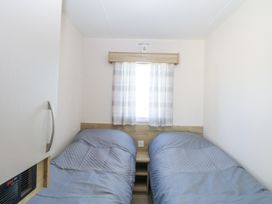 A bedroom with two single beds and a small window with curtains at 31A Foxburrow Hang in Fritton near Belton Norfolk
