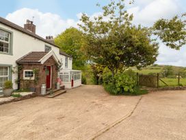 A house with a red door next to a tree and a fenced field at Kirkland Howe Cottage in Arlecdon