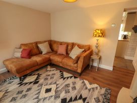A living room with a brown sectional sofa cushions a wooden side table with a lamp and a patterned rug on the floor at Kirkland Howe Cottage in Arlecdon