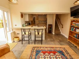 A kitchen and living area with stools at a counter a bookshelf a television and stairs at Kirkland Howe Cottage in Arlecdon