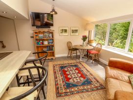 A room with a round wooden table and two chairs next to a large window a patterned rug on the floor a wooden bookshelf with books a mounted TV a brown leather sofa and two bar stools at a counter at Kirkland Howe Cottage in Arlecdon