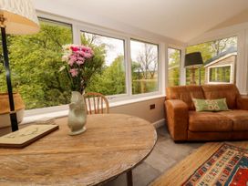 A room with a round wooden table with a vase of flowers a brown leather sofa and large windows at Kirkland Howe Cottage in Arlecdon