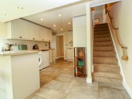 A kitchen with cabinets appliances and tiled floor next to carpeted stairs with a rope handrail at Kirkland Howe Cottage in Arlecdon