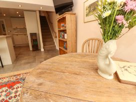 A dining area with a round wooden table holding a fish-shaped vase with flowers and a wooden chair near a bookshelf and stairs in Kirkland Howe Cottage Arlecdon