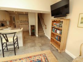 A kitchen area with a sink and chair and a wooden bookshelf with books beneath a wall mounted tv at Kirkland Howe Cottage in Arlecdon