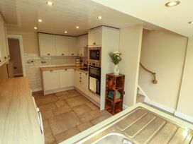 A kitchen with white cabinets a built in oven a wooden shelf with flowers and towels and a sink in the foreground at Kirkland Howe Cottage in Arlecdon