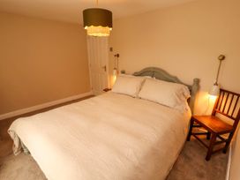 A bedroom with a bed with beige bedding a wooden chair a door and a hanging light at Kirkland Howe Cottage in Arlecdon