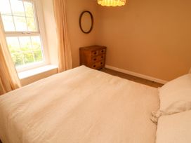 A bedroom with a bed covered in cream bedding a wooden chest of drawers a round mirror and window with curtains at Kirkland Howe Cottage in Arlecdon