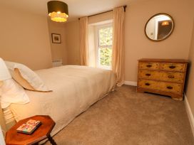 A bedroom with a bed a wooden chest of drawers a round mirror a side table and a window with curtains at Kirkland Howe Cottage in Arlecdon
