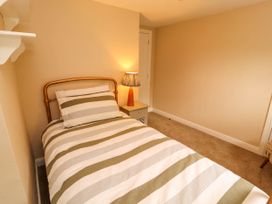 A bedroom with a single bed striped bedding a bedside table with a lamp and a door at Kirkland Howe Cottage in Arlecdon