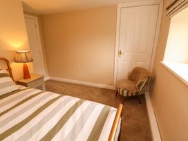A bedroom with a striped bedspread a bedside table with a lamp and a striped chair with a fur cover at Kirkland Howe Cottage in Arlecdon