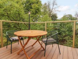 A wooden table with two green chairs on a balcony surrounded by trees at Kirkland Howe Cottage in Arlecdon