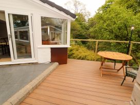 A wooden deck with a round table and chairs next to a house with sliding glass doors and trees in the background at Kirkland Howe Cottage in Arlecdon