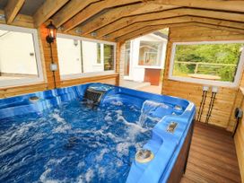 An indoor hot tub with water jets in a wooden room with windows showing an outdoor patio and greenery at Kirkland Howe Cottage in Arlecdon
