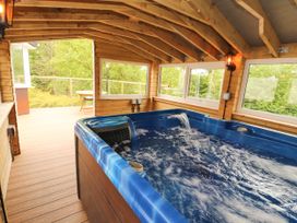 A covered wooden patio with a blue hot tub and large windows overlooking trees at Kirkland Howe Cottage in Arlecdon