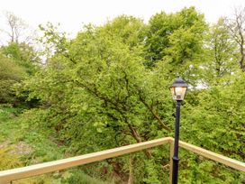 A balcony with a railing and a lit lamp post surrounded by green trees at Kirkland Howe Cottage in Arlecdon