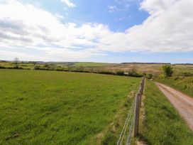 A rural landscape with green fields a dirt road and a wire fence at Kirkland Howe Cottage in Arlecdon