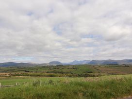 A rural landscape with green fields hills and mountains under a partly cloudy sky at Kirkland Howe Cottage in Arlecdon